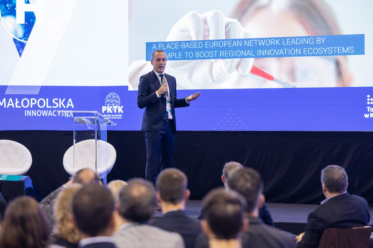 Řečník na pódiu konference Polského klastru kompozitů (PKTK), v pozadí promítaná prezentace